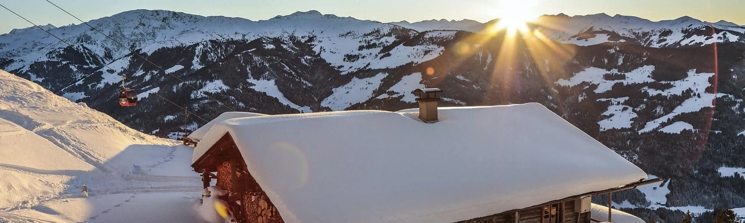Sonnenaufgang hinter einer Berghütte in einer schneebedeckten Landschaft