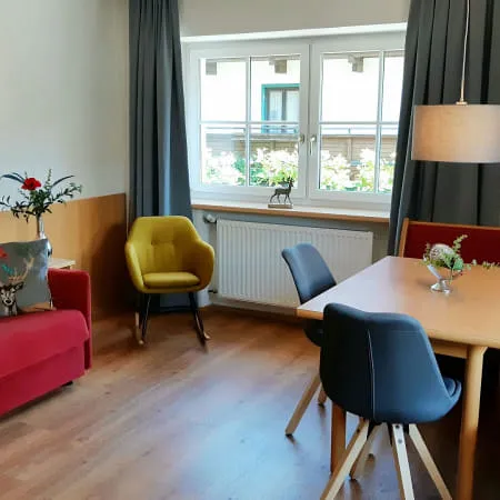 Gemütlicher Wohnraum mit rotem Sofa, Esstisch und großen Fenstern