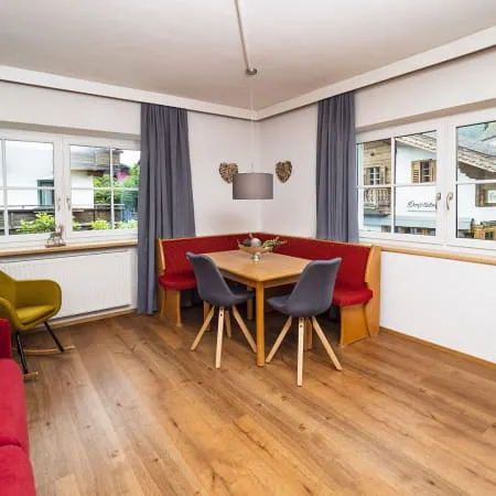 Heller Innenraum mit Holzboden, Sitzbereich und Esstisch neben großen Fenstern.