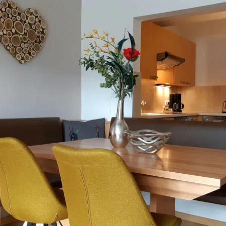 Helles Wohnzimmer mit Esstisch und Küche im Hintergrund.